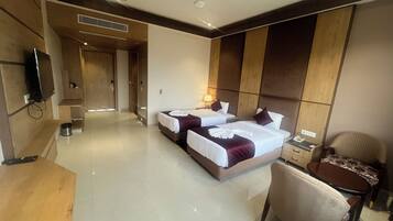 A hotel room with two beds, a desk, a chair, a TV, and a bathroom.
