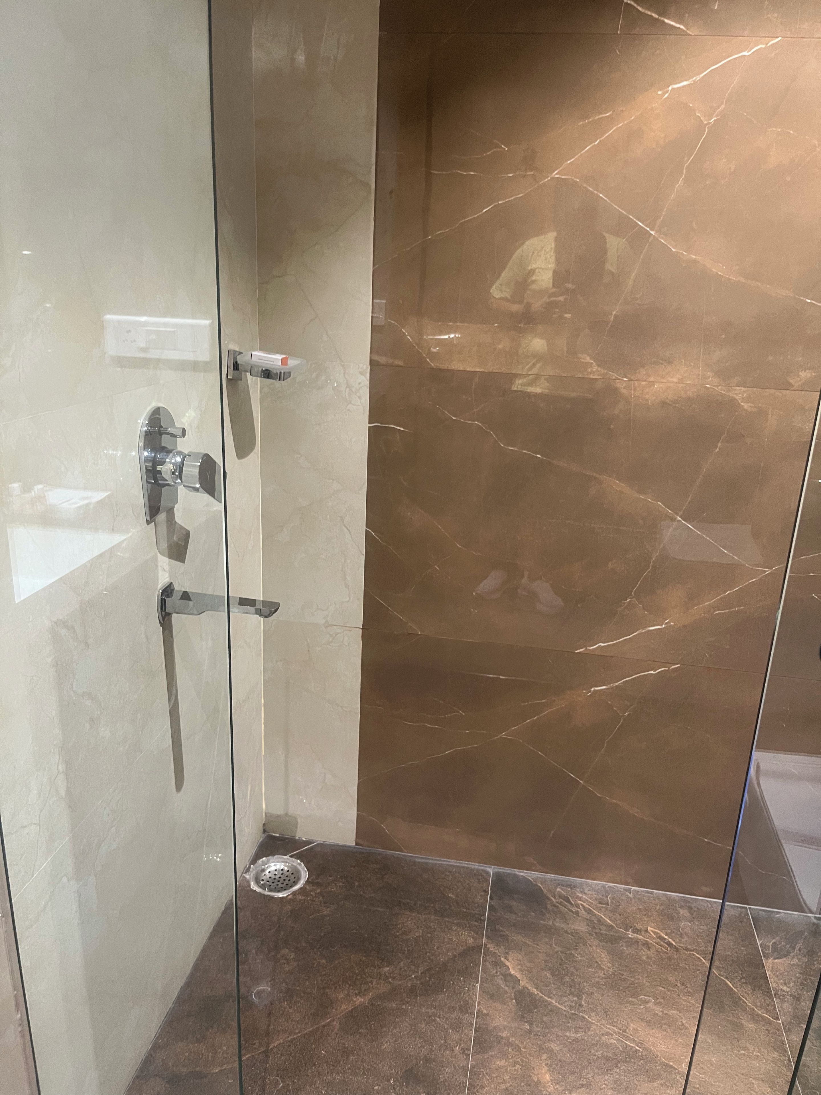 A glass-enclosed shower with a marble floor and a wall-mounted faucet.