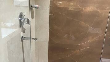A glass-enclosed shower with a marble floor and a wall-mounted faucet.