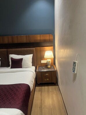 Una habitación de hotel con una cama, una mesita de noche con una lámpara y un enchufe de pared.