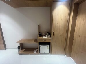 A compact room with a wooden wardrobe, a small desk, and a white refrigerator. - Nirvana Grand Hotel And Resort (Gaya)