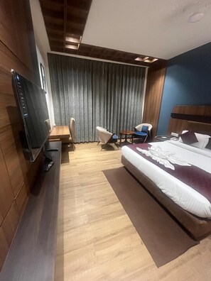 Une chambre d’hôtel avec un lit, un bureau, une chaise, une télévision et un rideau.