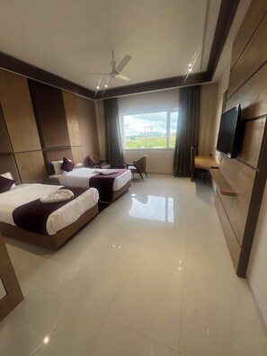 A modern hotel room with two beds, a TV, a ceiling fan, and a large window offering a view of the outdoors. - Nirvana Grand Hotel And Resort (Gaya)