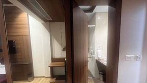 Una camera d'hotel con pavimento in legno, una piccola panca in legno, un box doccia in vetro e un lavandino con un asciugamano appeso al muro.