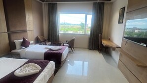 Camera d'albergo con due letti, una scrivania, una sedia, una televisione e una finestra vista campagna.