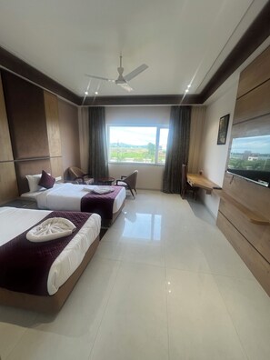 A hotel room with two beds, a desk, a chair, a TV, and a window with a view of the countryside. - Nirvana Grand Hotel And Resort (Gaya)