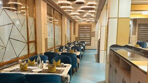 Un'ampia sala da pranzo con tavoli apparecchiati per numerosi ospiti, caratterizzata da un design moderno, sedie imbottite blu e un'isola centrale con bancone.