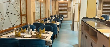 Une grande salle à manger avec des tables disposées pour accueillir de nombreux convives, présentant un design moderne avec des chaises recouvertes de tissu bleu et un îlot central doté d’un comptoir.