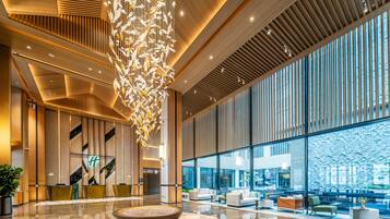 A modern lobby with a central seating area, a decorative hanging installation, and large windows offering views.