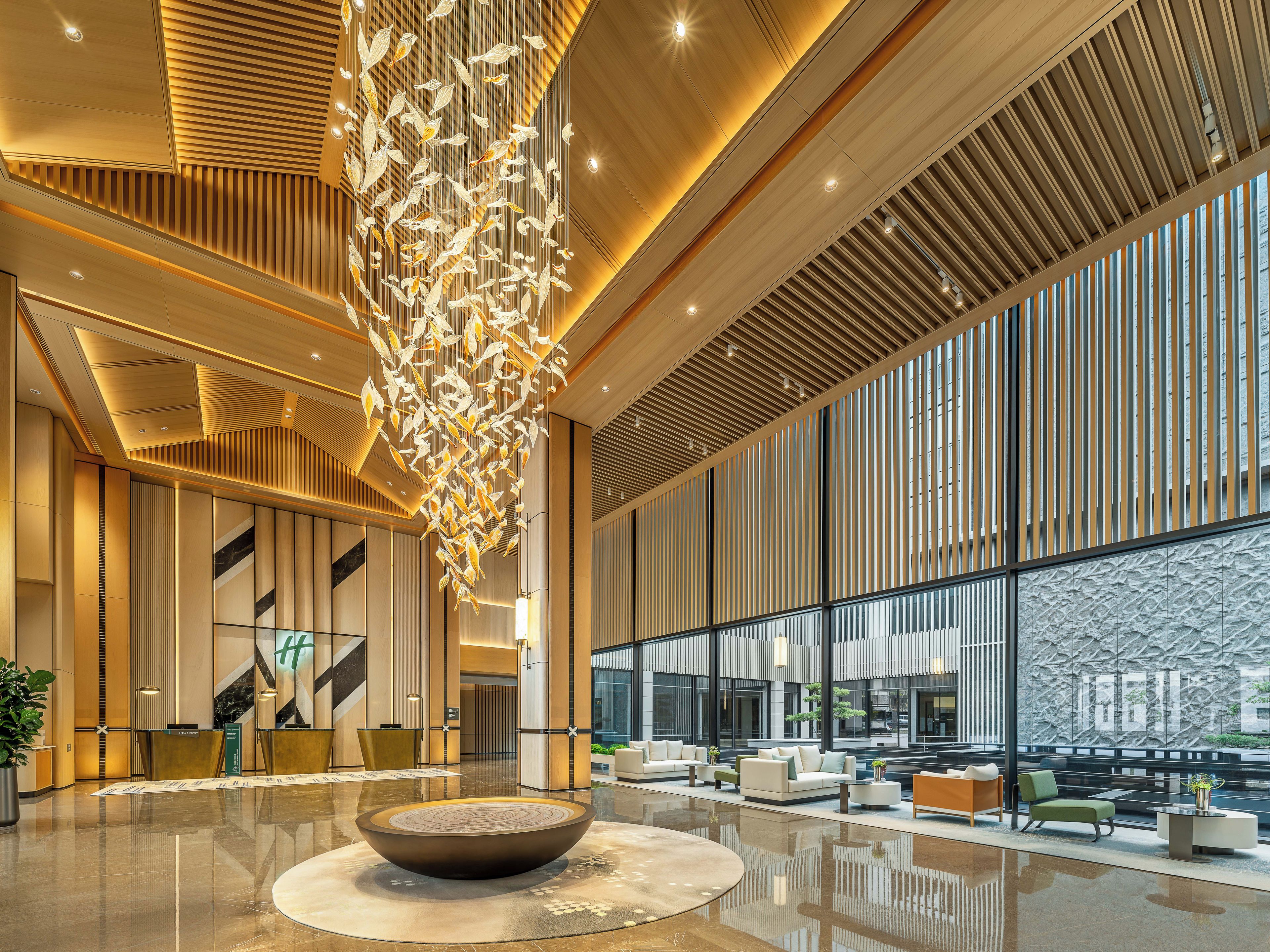 A modern lobby with a central seating area, a large decorative light fixture, and a reception desk.