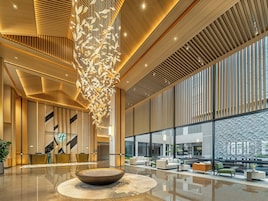 A modern lobby with a central seating area, a large decorative light fixture, and a reception desk.