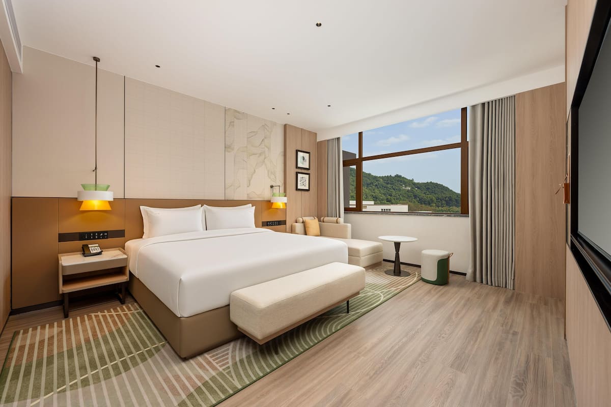 Ein Hotelzimmer mit einem großen Bett, Nachttischen, einer Bank, einem kleinen Tisch und Blick ins Freie.