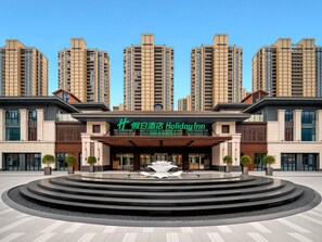 Un hôtel à la façade moderne, doté d’une entrée centrale et d’une fontaine à l’avant.