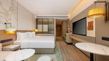 A modern hotel room with a bed, a TV, a desk, and a seating area.