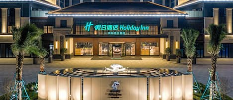 A Holiday Inn with a traditional architectural style, featuring a central courtyard with a fountain, palm trees, and a well-lit entrance.