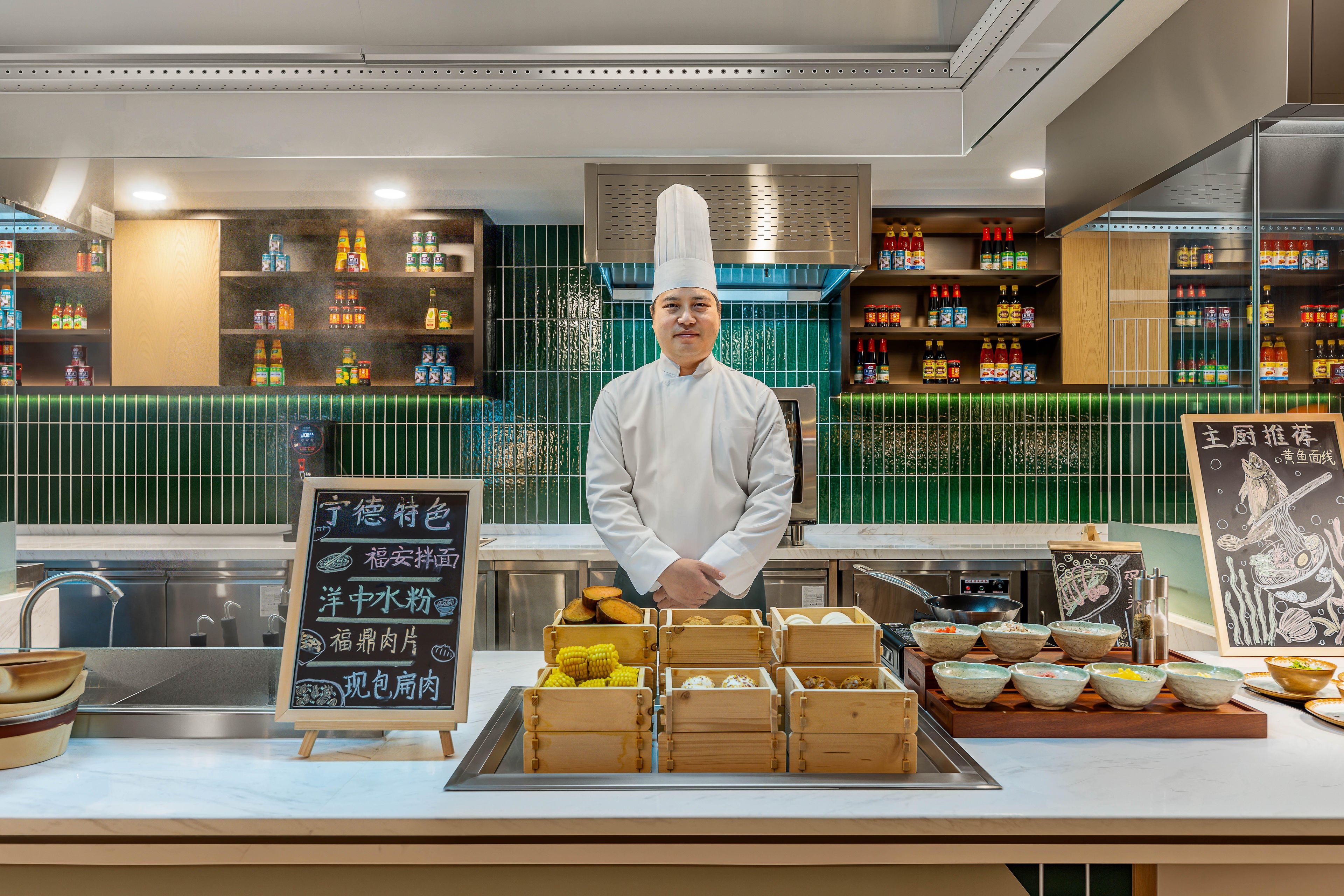 A chef standing behind a counter with various food items and condiments.