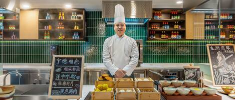 A chef standing behind a counter with various food items and condiments.