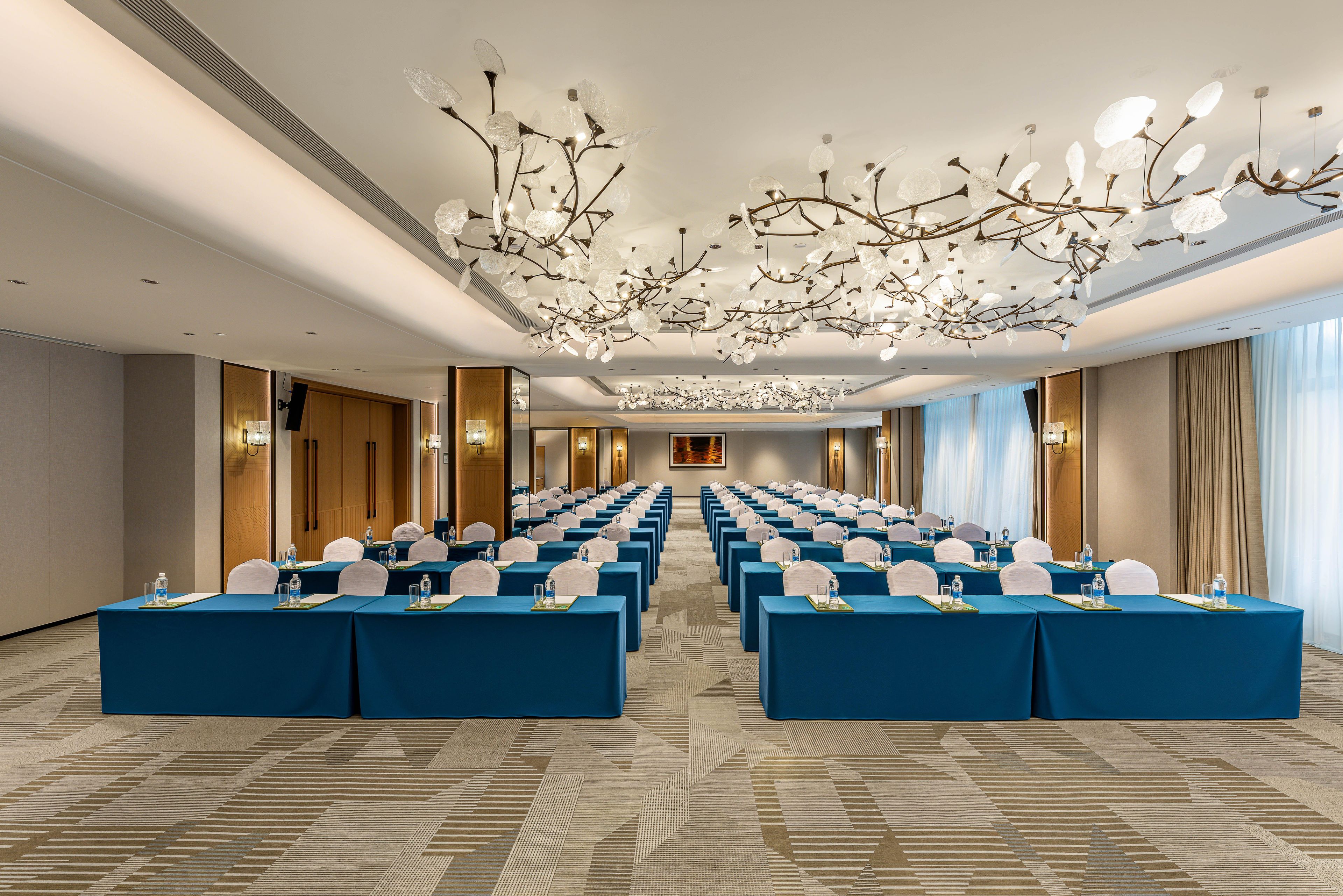 A conference room with rows of tables, chairs, and a modern chandelier.