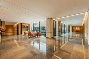 Un vestíbulo amplio con piso de mármol pulido, muebles modernos y ventanas grandes que ofrecen vistas al exterior.