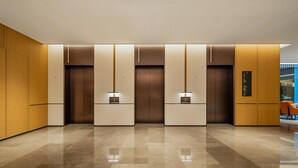 Un área de ascensor moderna con suelo de mármol pulido, paneles de madera y paneles de pared iluminados.