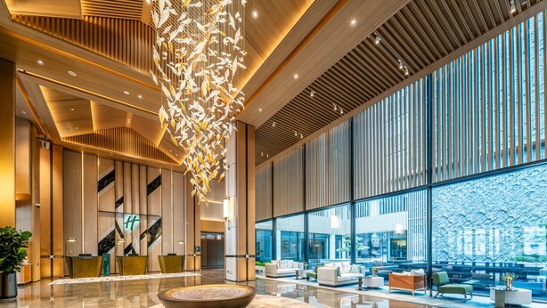 Eine moderne Lobby mit einer zentralen Sitzgruppe, einer dekorativen Hängekonstruktion und großen Fenstern mit Blick.