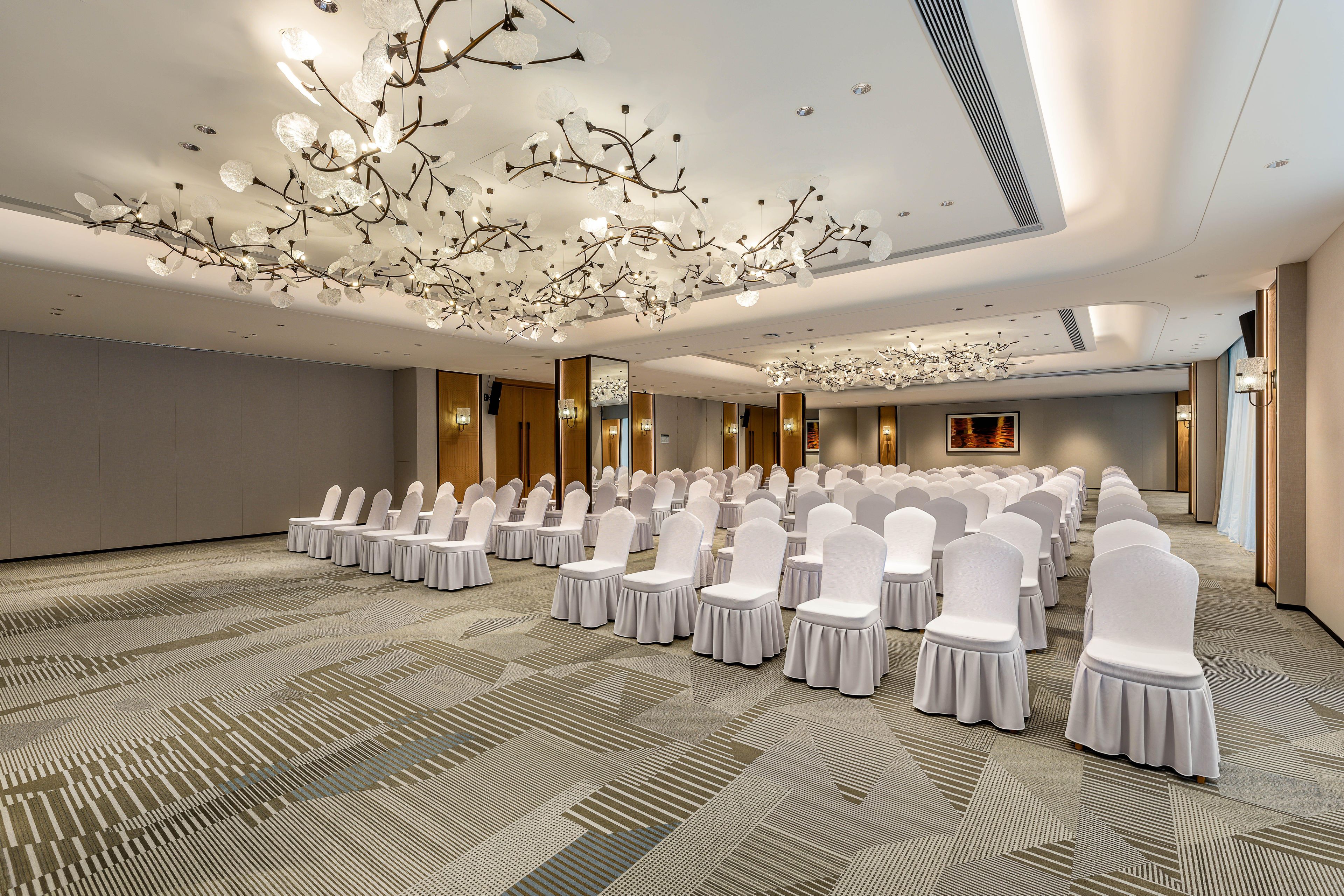 A conference room with rows of white chairs, a patterned carpet, and a modern chandelier.