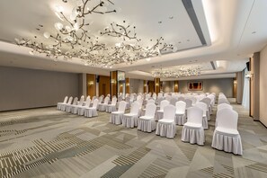 Un salón de conferencias con filas de sillas blancas, una alfombra estampada y una lámpara de araña moderna.