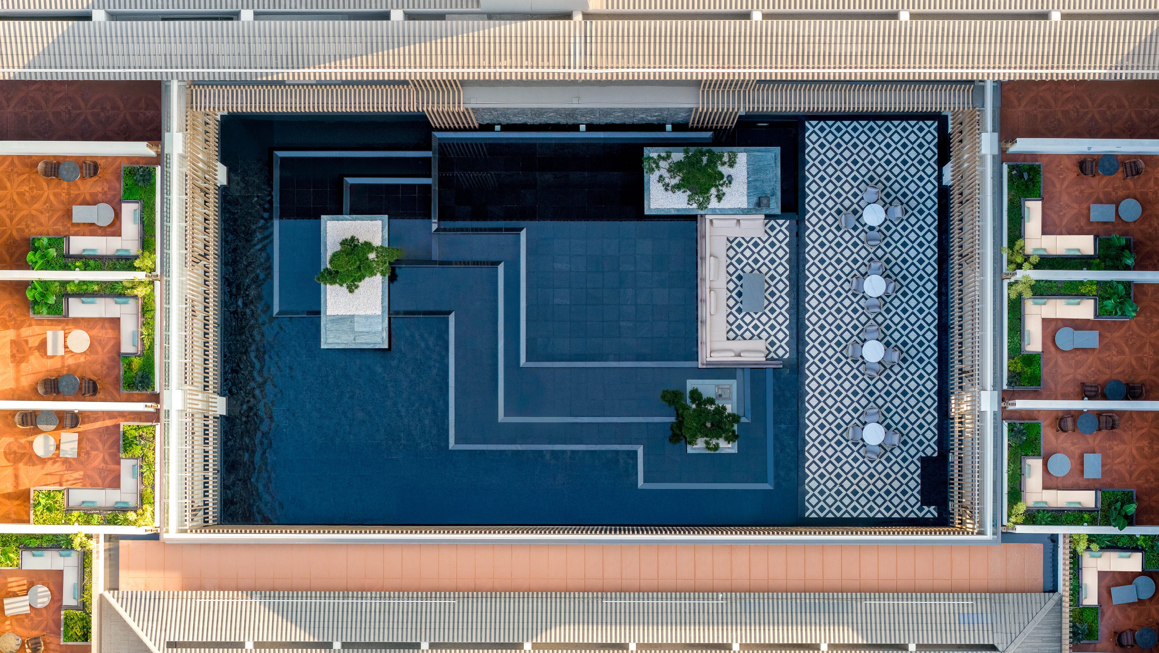 Vue aérienne d’une terrasse sur le toit, avec des aménagements de sièges aux formes géométriques, une fontaine centrale et une végétation luxuriante tout autour.
