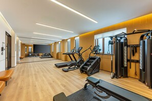 Un gimnasio con máquinas de cardio, equipo de levantamiento de pesas y bancos.
