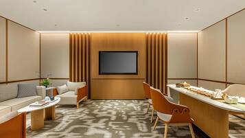 A modern hotel room with a flat-screen TV, a sofa, a dining table, and a patterned carpet.