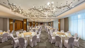 A banquet hall with round tables, white chairs, and a decorative ceiling.