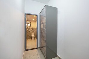 A narrow hallway leading to a bathroom with a toilet, shower, and tiled walls. - Alaya Stays By Elivaas Lake City Heights (Udaipur)
