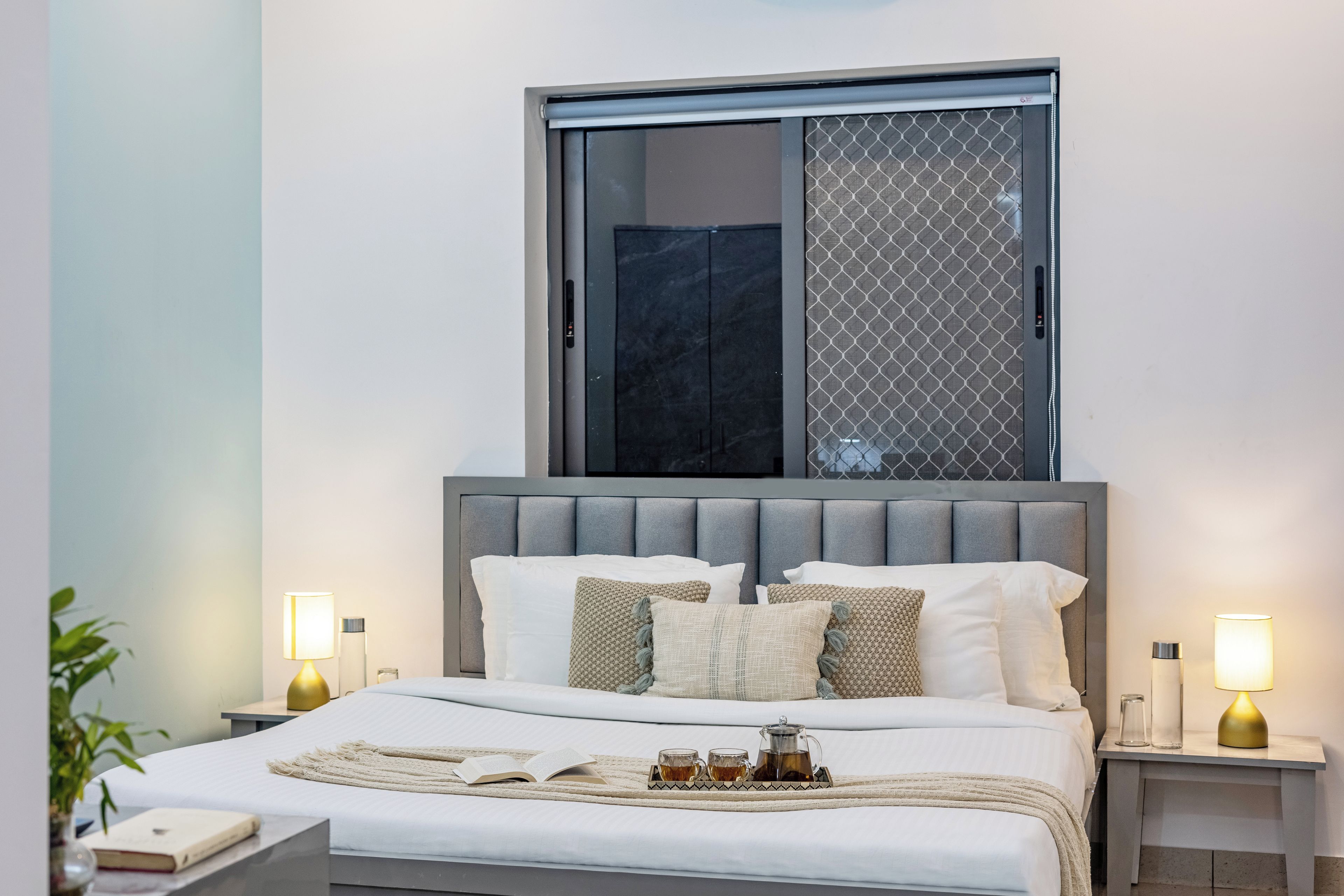 Un dormitorio moderno con una cama grande, dos mesitas de noche, un ventanal con vistas y una bandeja con té y azúcar.
