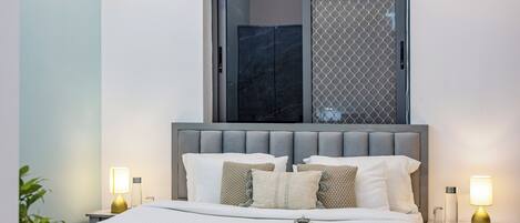 A modern bedroom with a large bed, two bedside tables, a window with a view, and a tray with tea and sugar.