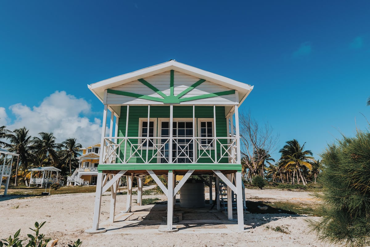 A beachside lifeguard tower with a green and white color scheme, situated on a sandy beach with palm trees in the background.