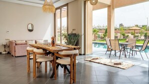 Ein geräumiges Wohnzimmer mit einem Holzespeisetisch und Stühlen, einem Sofa und Blick auf einen Swimmingpool und Garten.