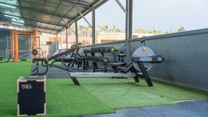 A gym with exercise equipment, artificial grass flooring, and a covered area with a metal roof. - Life Resort (Marrakech)