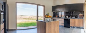 A modern kitchen with a large island, dark cabinetry, and a view of a desert landscape through a sliding glass door. - Life Resort (Marrakech)