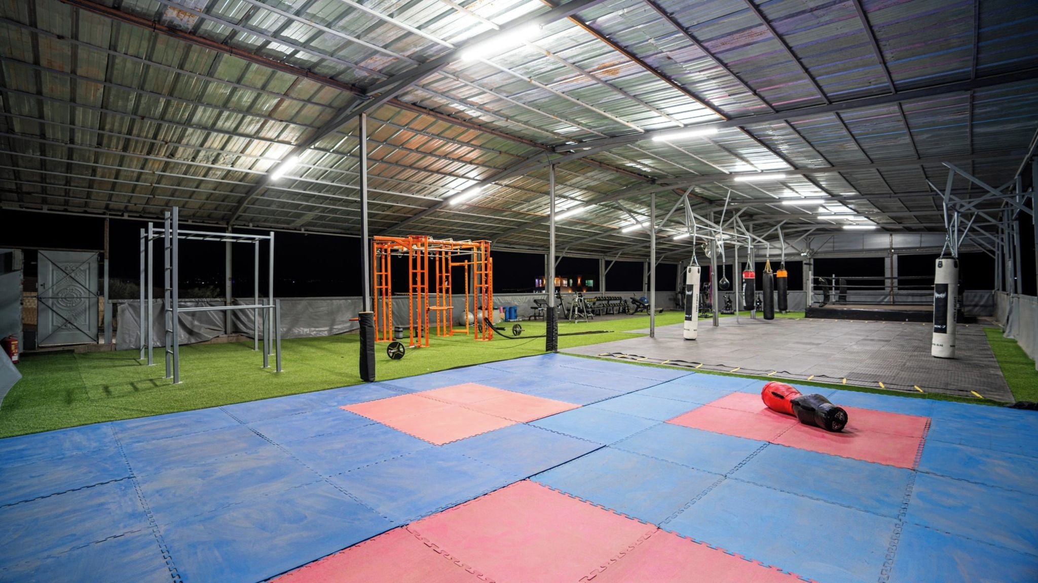 Een binnengymzaal met diverse fitnessapparaten, kunstgras en geveerde matten.