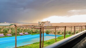 A pool area with lounge chairs and a view of a modern building in a desert landscape. - Life Resort (Marrakech)