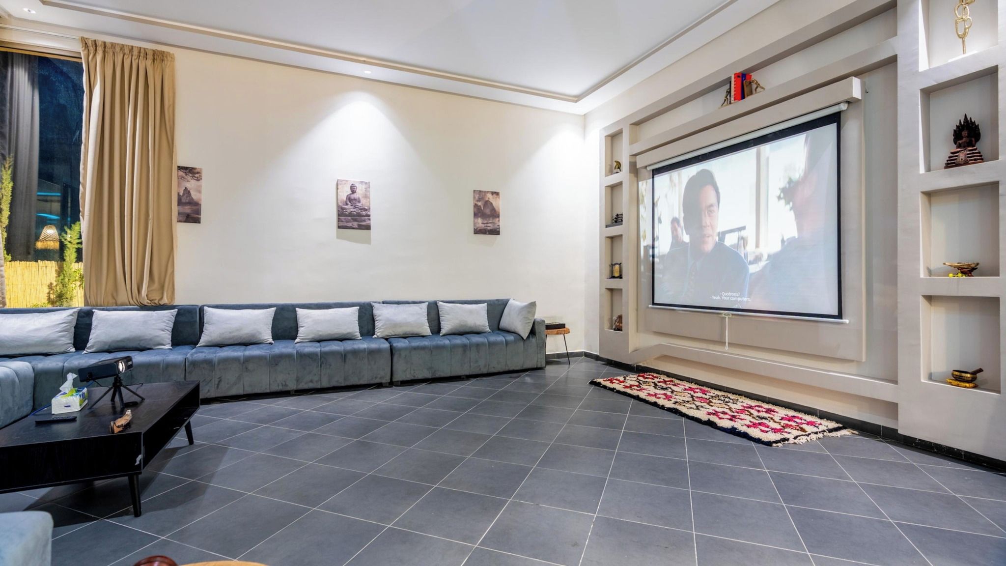 Una sala de estar moderna con un sofá gris, un televisor de pantalla plana montado en la pared y una pequeña mesa de centro.