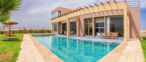 Une maison moderne dotée d’une piscine, de grandes fenêtres et d’un espace salon extérieur.