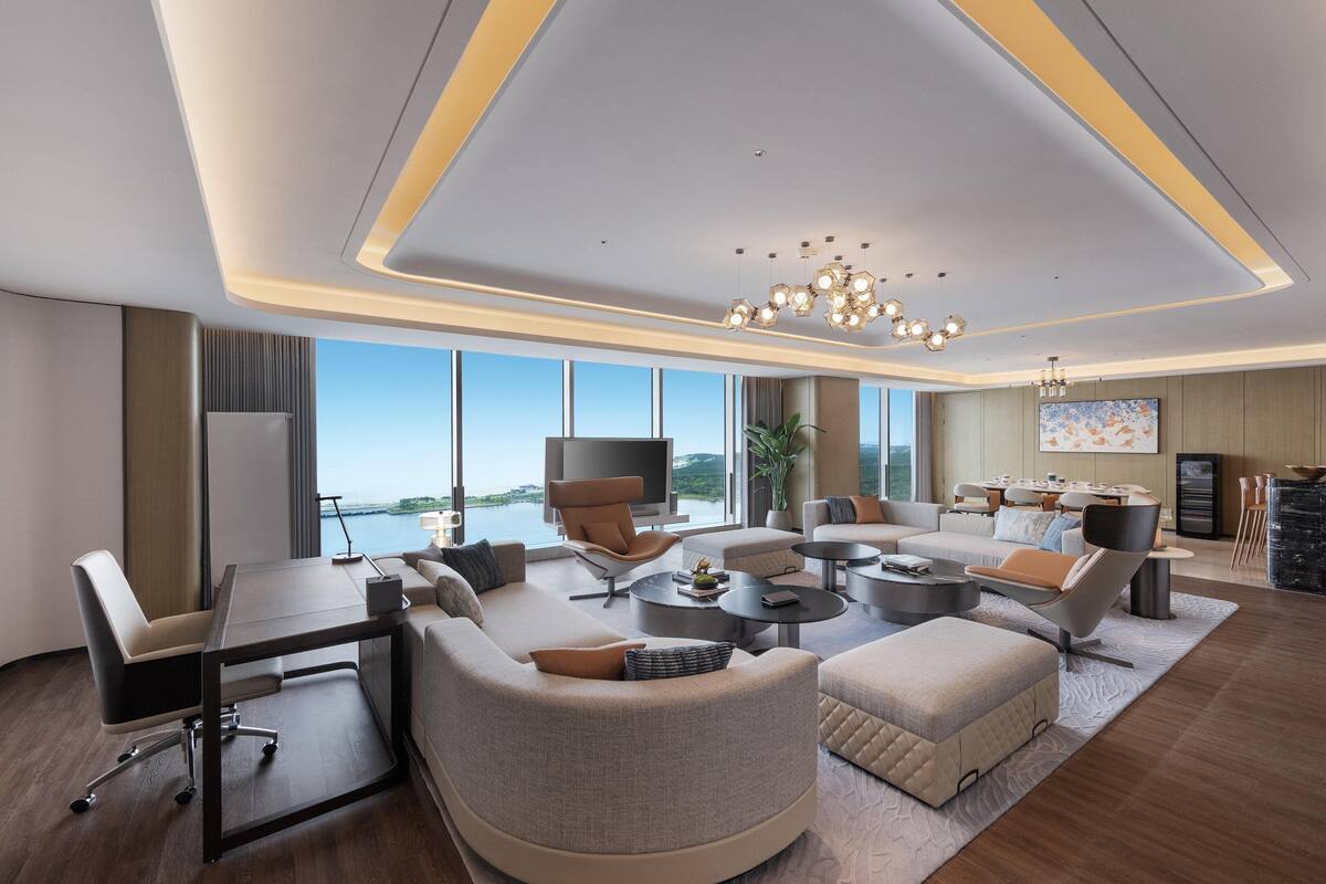 Une chambre d’hôtel moderne dotée d’une grande fenêtre, d’une table basse ronde, d’un canapé, d’une télévision et d’un coin repas.