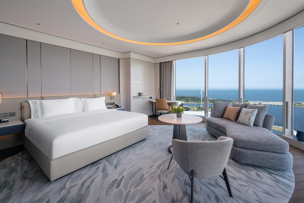 Une chambre d’hôtel moderne avec un grand lit, un canapé, une petite table et une vue sur l’océan.