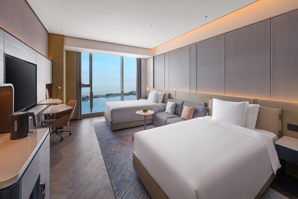 Une chambre d’hôtel avec un grand lit, un lit plus petit, un bureau, une chaise et un téléviseur.