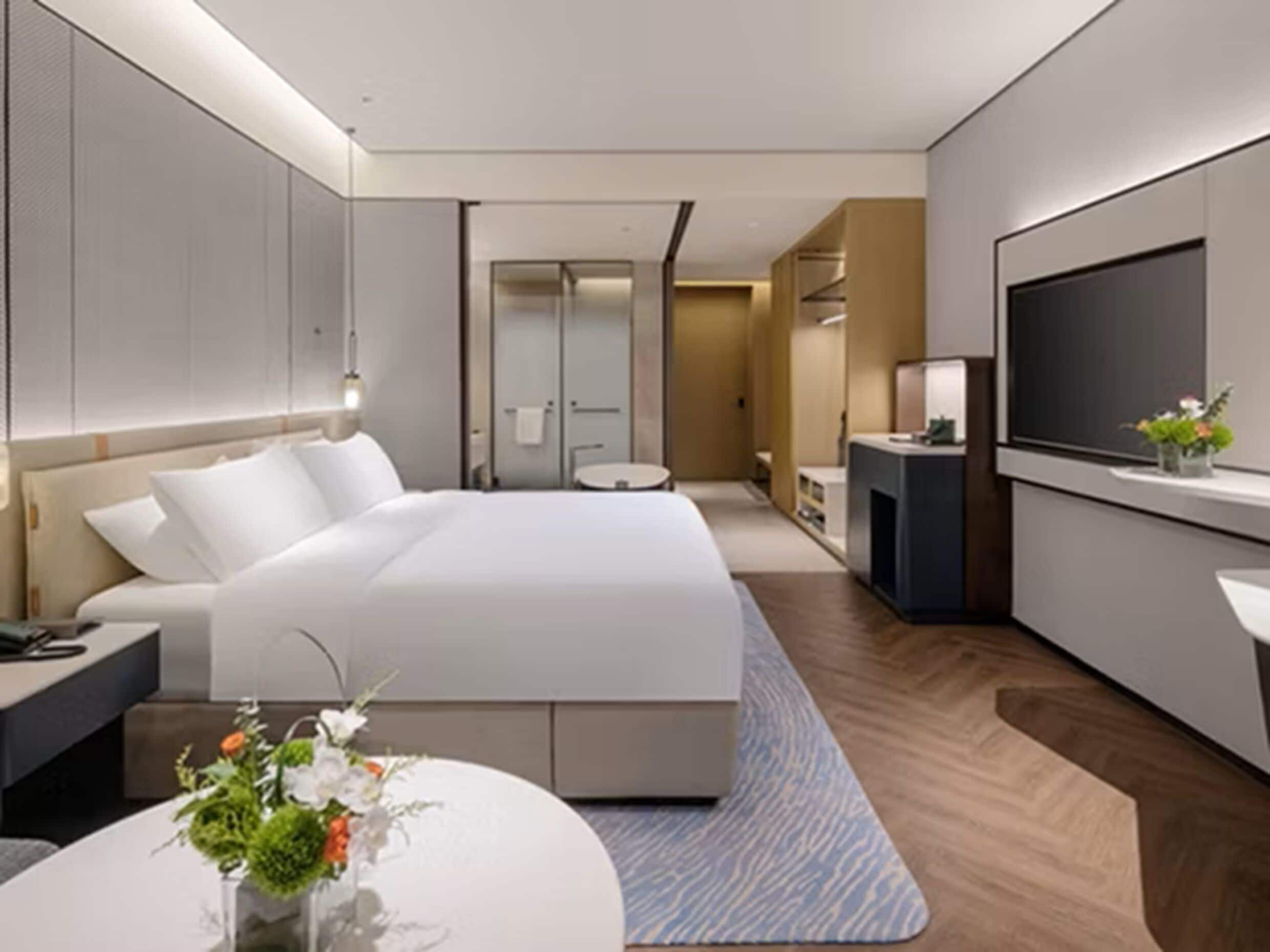 Una habitación de hotel moderna con una cama grande, un escritorio, un televisor y un baño visible a través de una puerta de cristal.