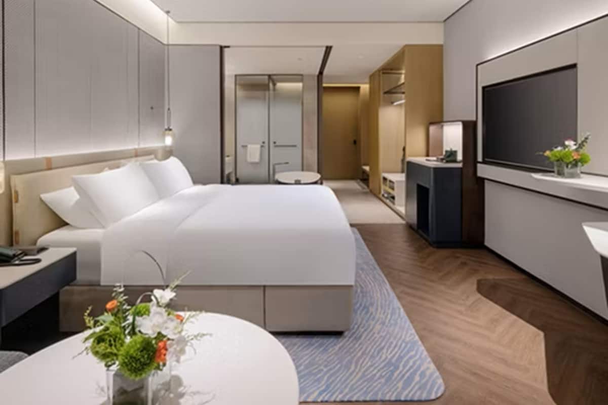 Une chambre d’hôtel moderne dotée d’un grand lit, d’un bureau, d’une télévision et d’une salle de bain visible à travers une porte en verre.