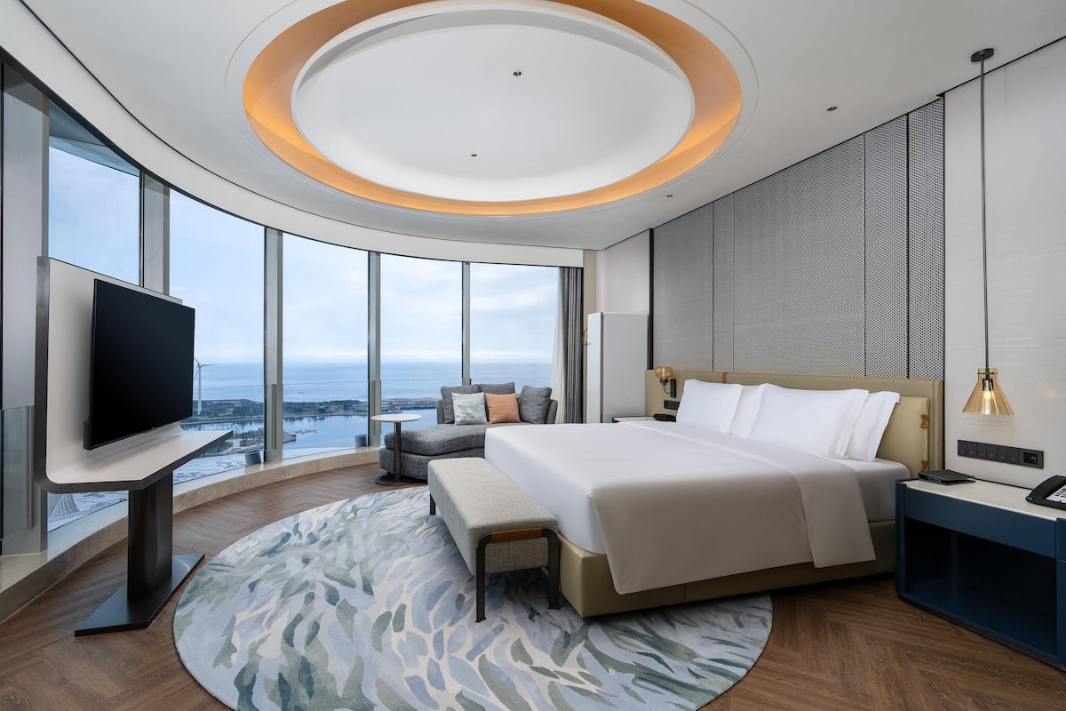 Une chambre d’hôtel moderne dotée d’un grand lit, d’une télévision à écran plat, d’un bureau et offrant une vue sur l’océan.