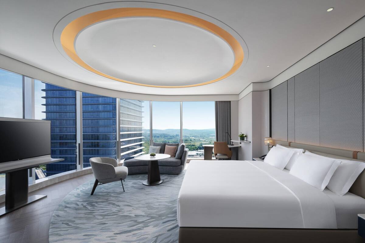 Une chambre d’hôtel moderne dotée d’un grand lit, d’un coin salon avec une table, d’une télévision et offrant une vue sur la ville.