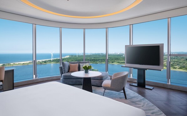Une chambre d’hôtel moderne dotée d’un grand lit, d’une télévision et offrant une vue sur la mer et les éoliennes.